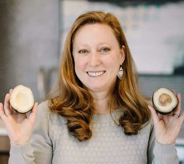 Erika Hewlett, FNTP, holding up an avocado cut open into halves.