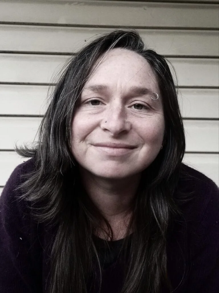 Smiling woman with long dark hair and facial piercings